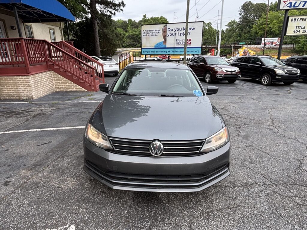 Gray Volkswagen in the foreground of a parking lot, with a brick building and red railing to the left and a large billboard in the background.