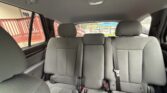 Interior view of a car's rear row with three grey seats and visible seat belts; outside shows a red railing and parking area.