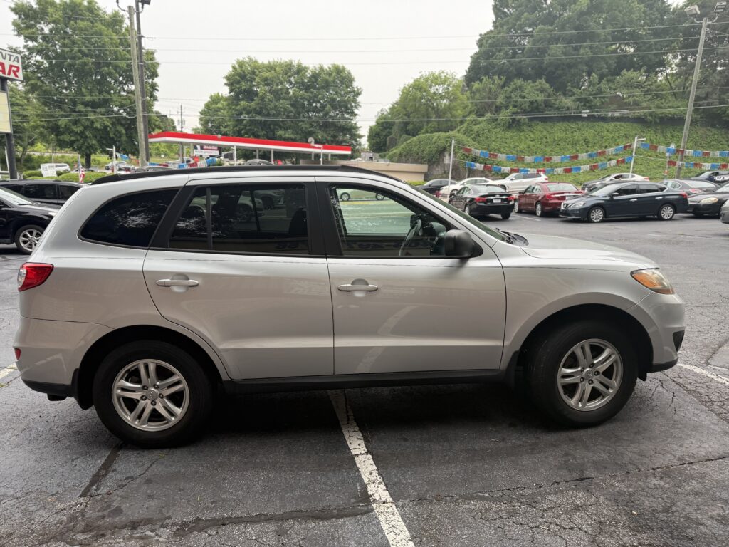Silver SUV in the foreground parked in a busy lot with colorful banners and trees in the background.