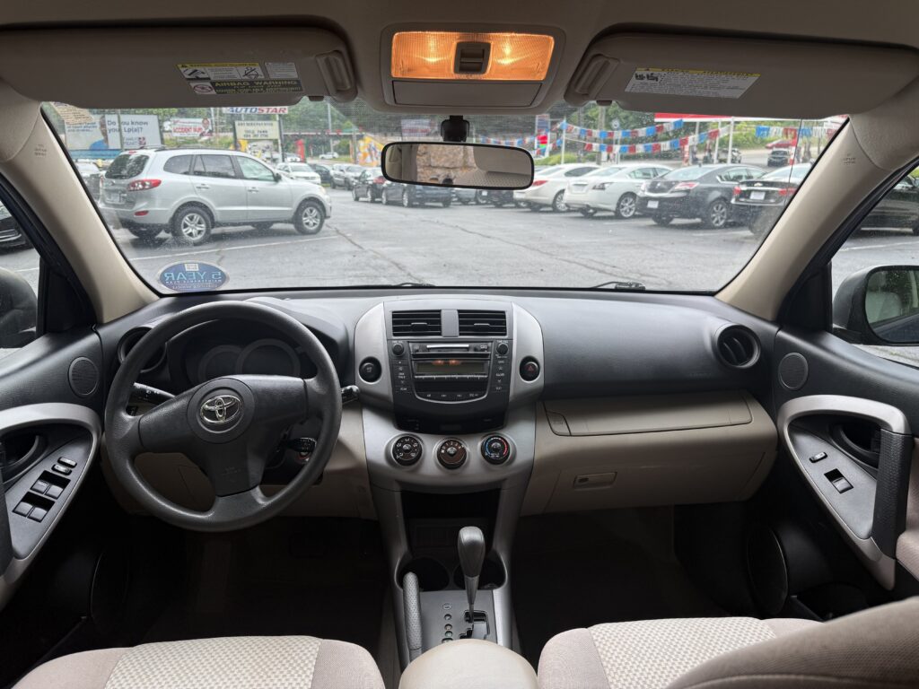View from driver seat: dashboard, steering wheel, center console, and gear shifter with a busy parking lot outside the windshield.