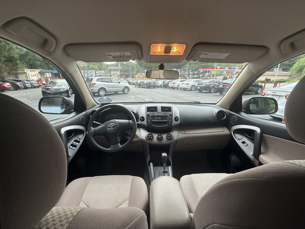 View from the back seat looking toward the front of a parked SUV, with the dashboard and center console visible and a busy car lot outside the windows.