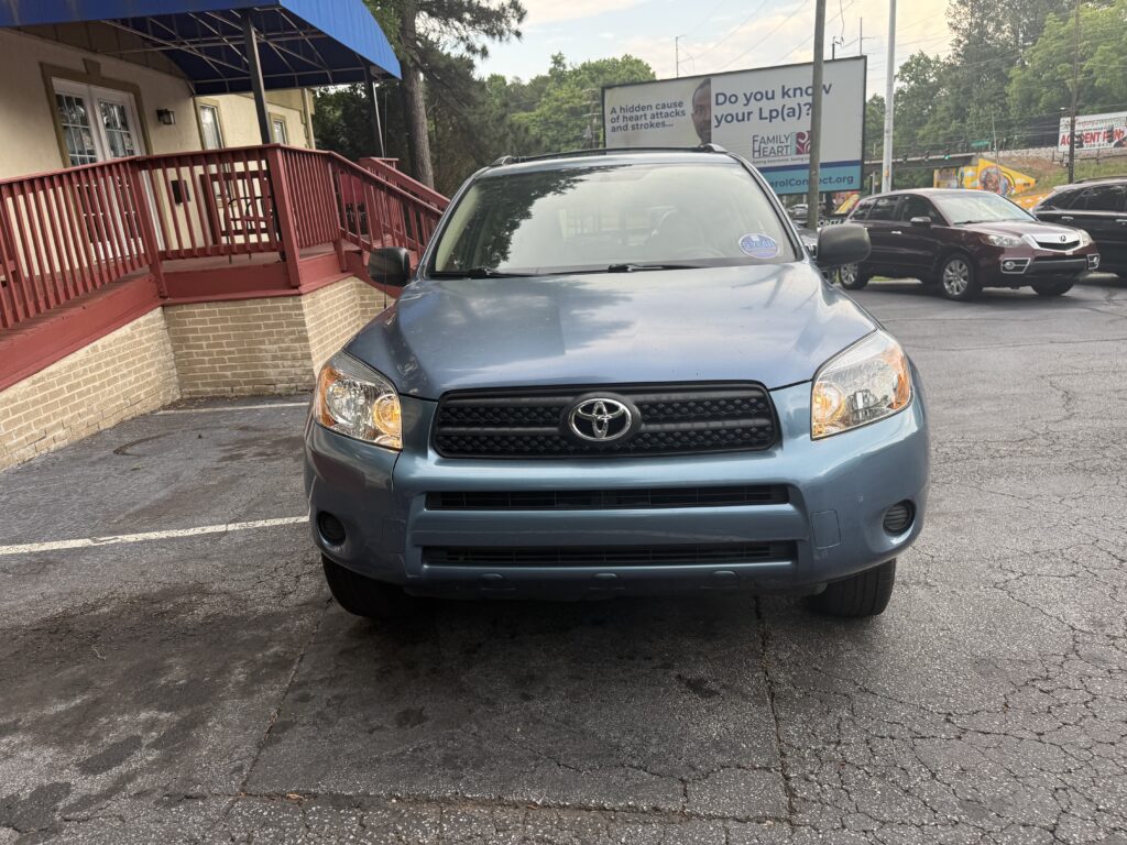 Front view of a blue Toyota SUV parked in a lot beside a brick building with a red railing and blue awning on the left.”,