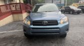 Front view of a blue Toyota SUV parked in a lot beside a brick building with a red railing and blue awning on the left.”,