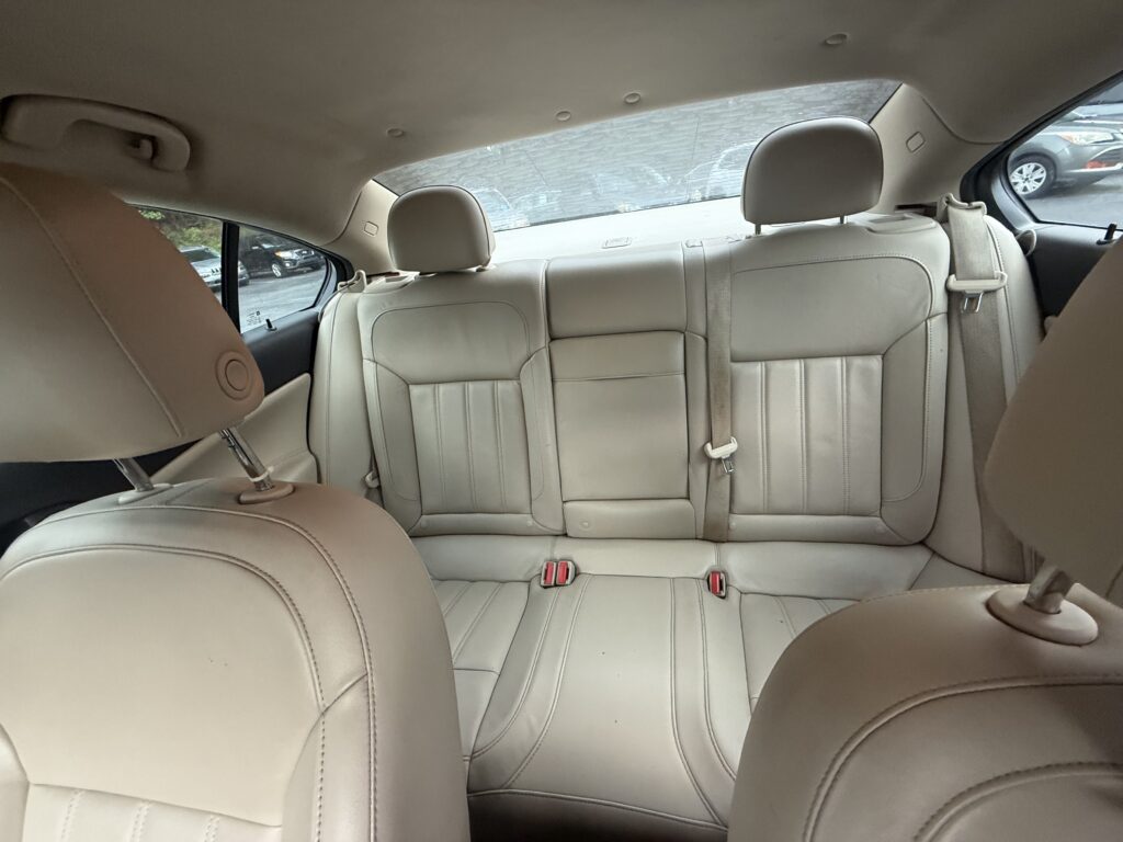 Rear interior of a beige leather car showing back seats, headrests, and visible seat belts.