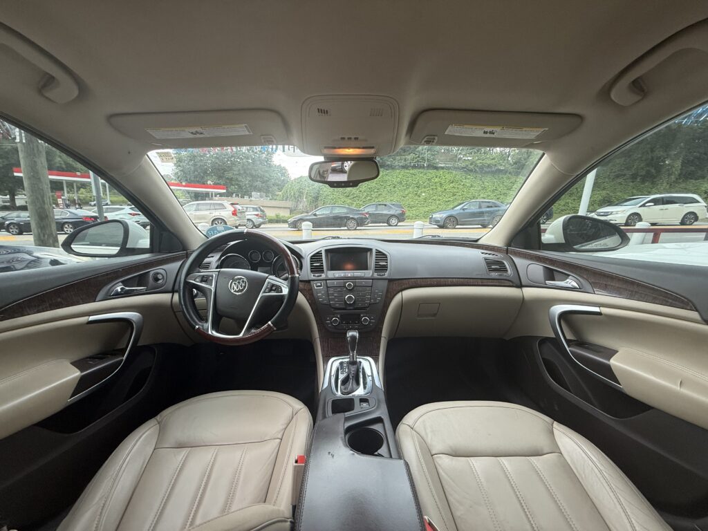 Interior of a beige leather SUV cabin, showing the steering wheel, center stack, and front seats with a parking lot outside the windshield.