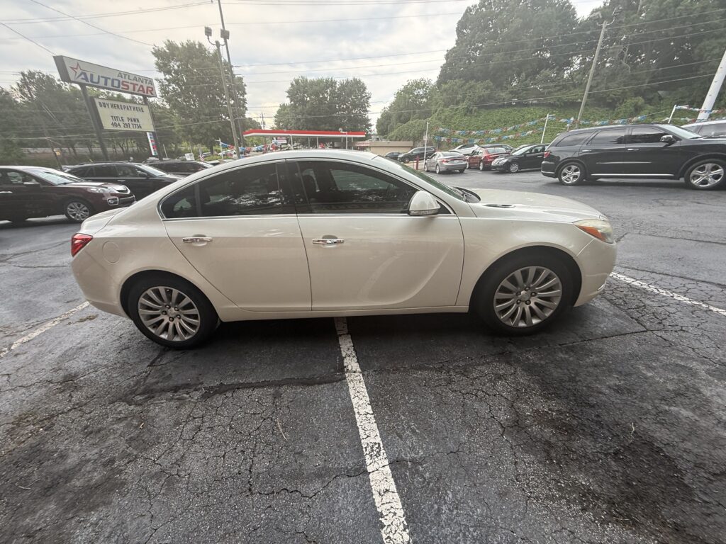 Beige sedan parked in a crowded parking lot with other cars and a dealership sign in the background. Overcast sky.