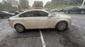 Beige sedan parked in a crowded parking lot with other cars and a dealership sign in the background. Overcast sky.