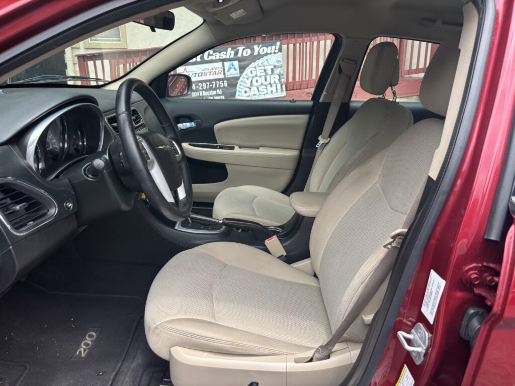 Front interior of a red car with beige cloth seats, steering wheel, and center console gear shifter visible.