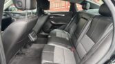 Rear passenger seating area of a black leather car interior with two headrests and visible seatbelts. The door panel and wood trim are also shown.