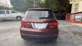 Rear view of a maroon Acura MDX SUV parked in a lot, showing the dealership plate frame and surrounding cars in the background.