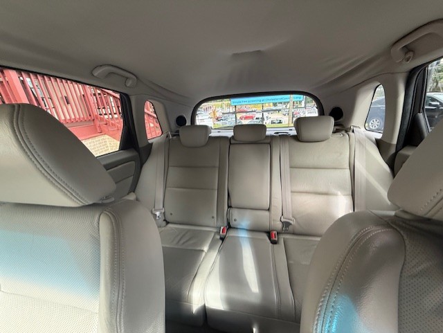 Back seat of a beige leather car interior with three headrests and visible seat belts, seen from the front passenger area.