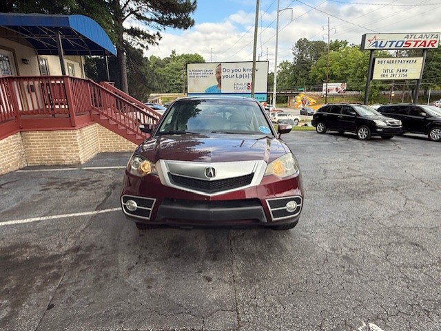 Maroon Acura SUV photographed from the front in a car dealership lot, with signs and other vehicles visible in the background.