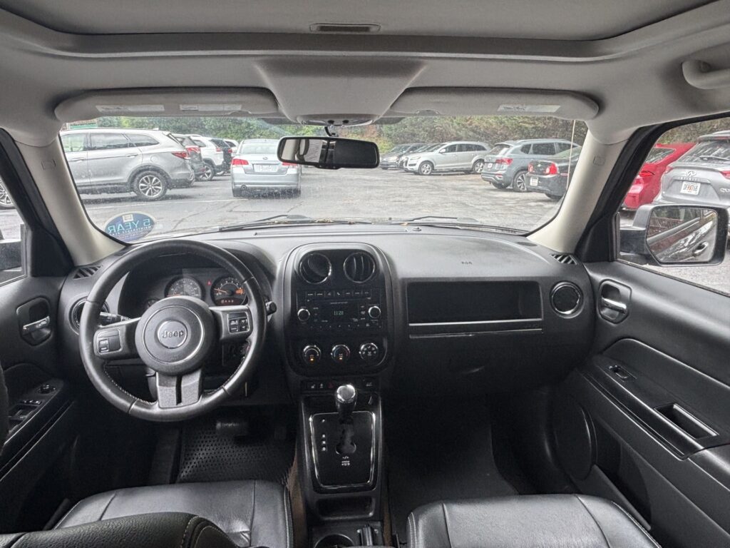 View from the back seat of a Jeep: front dashboard, steering wheel, center console, and rearview mirror with a parking lot of cars outside the windshield.