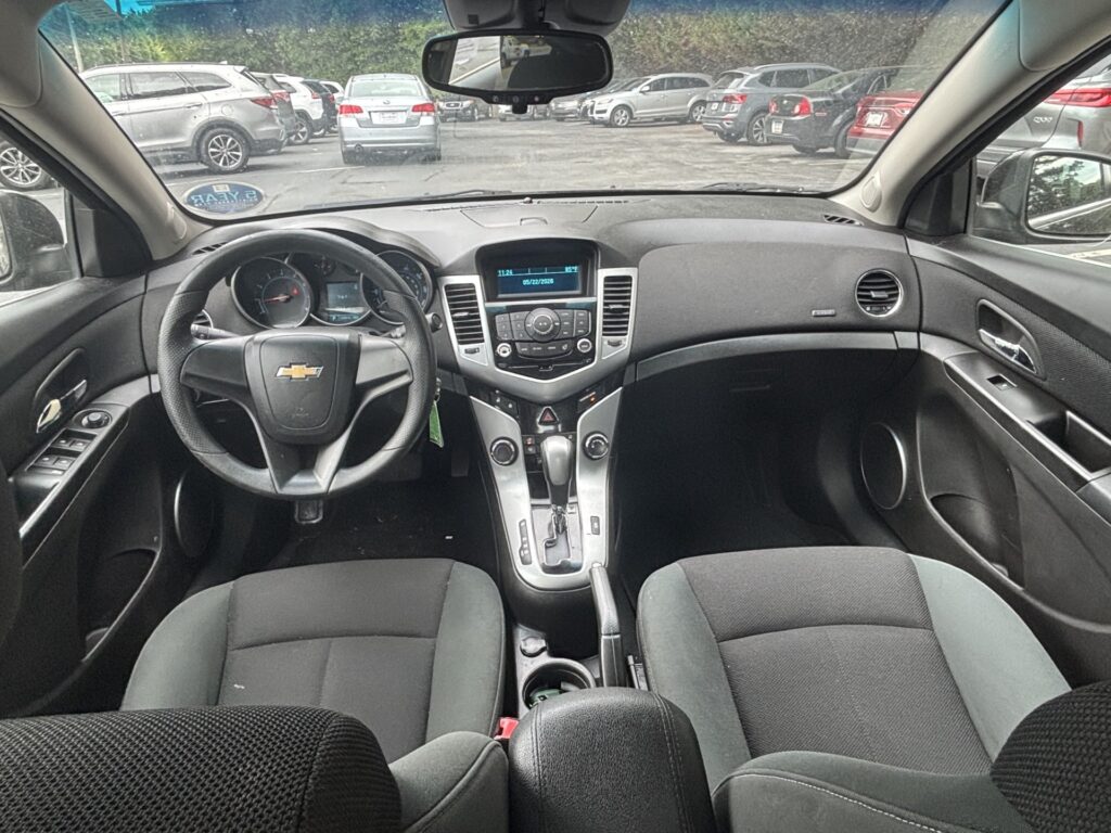 Inside a Chevrolet car’s front cabin, view from the center area of the dashboard facing the windshield and parked cars ahead.