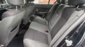 Rear interior of a dark fabric sedan: back seats with headrests, seat belts, and door panel visible through an open door edge.