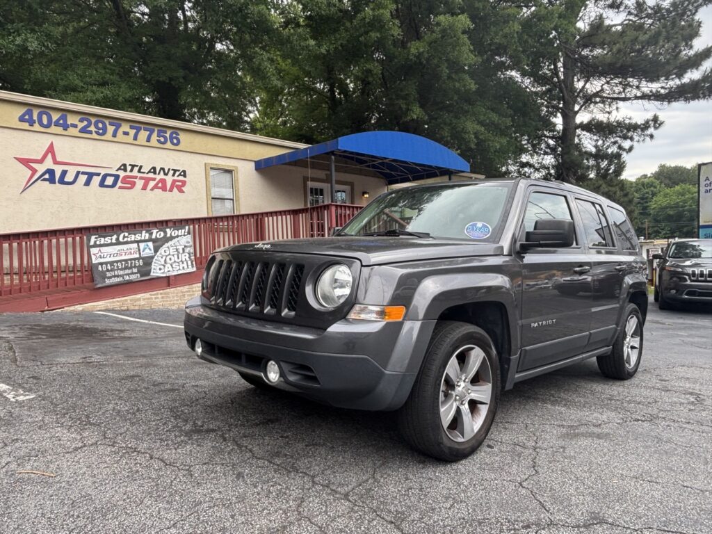 Gray Jeep Patriot parked in front of Atlanta AutoStar dealership under a blue awning. The building displays the 'Atlanta AutoStar' sign and posters in the foreground.