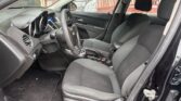 Interior of a black car showing driver's seat, steering wheel, and front passenger seat viewed from open driver-side door; dusty floor mats visible outside window at a drive-through area.