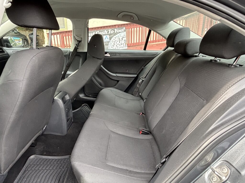 Rear seats of a dark fabric sedan with headrests and seatbelts; outside window shows a sign reading 'Get Your Cash'.