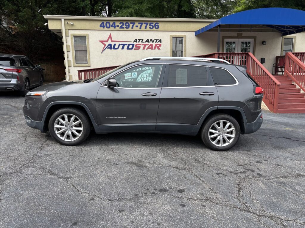 Gray Jeep Cherokee SUV parked in front of a beige storefront with 'Atlanta Auto Star' sign and large blue phone number above it; a wooden ramp and blue canopy are on the right.