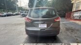 Rear view of a gray Ford Escape SUV parked in a parking lot, dealership plate frame, with a red railing and building to the right.