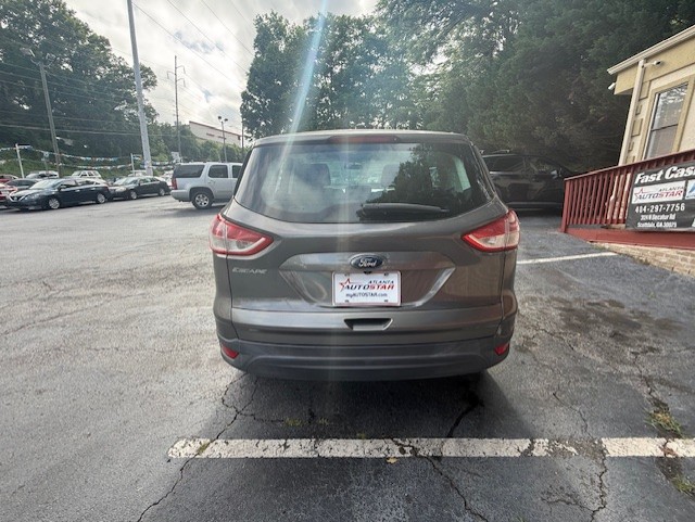 Rear view of a gray Ford Escape SUV parked in a parking lot, dealership plate frame, with a red railing and building to the right.