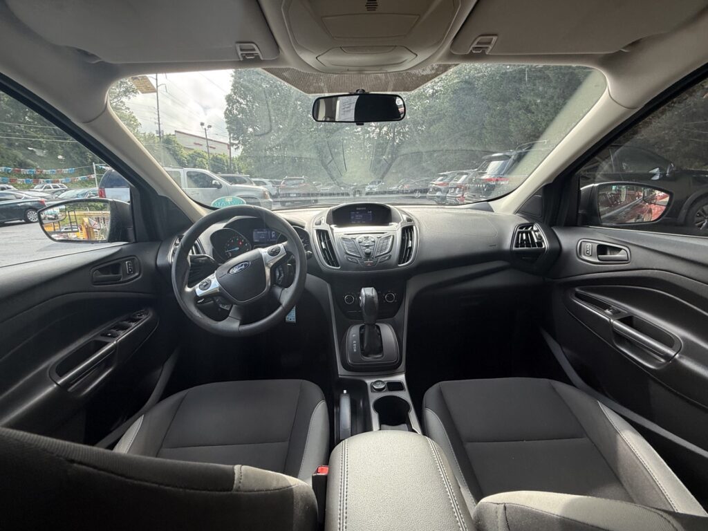 Interior of a car cabin viewed from the back seat, showing steering wheel, center console, gear shifter, and front dashboard.