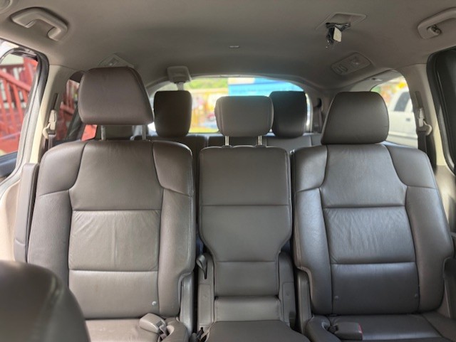 Interior of a black leather minivan showing three rows of seats, with two captain's chairs in the middle row and a center aisle view to the back.