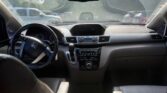 Interior of a car: dashboard and steering wheel viewed from the back seat, with the center console, rearview mirror, and cupholders visible.