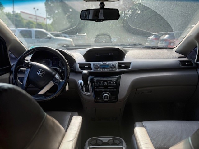 Interior of a car: dashboard and steering wheel viewed from the back seat, with the center console, rearview mirror, and cupholders visible.