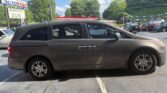 Side view of a gray minivan parked in a car dealership lot, with Atlanta AutoStar signage in the background.