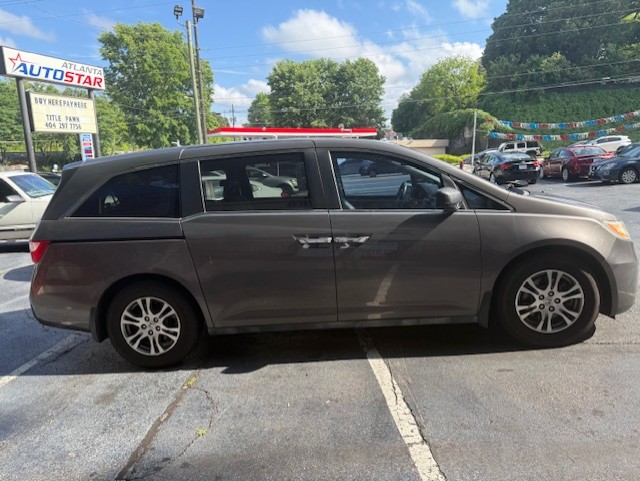 Side view of a gray minivan parked in a car dealership lot, with Atlanta AutoStar signage in the background.
