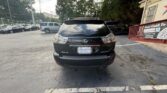 Rear view of a black Lexus SUV parked in a car lot, license plate visible, with trees and a building in the background.