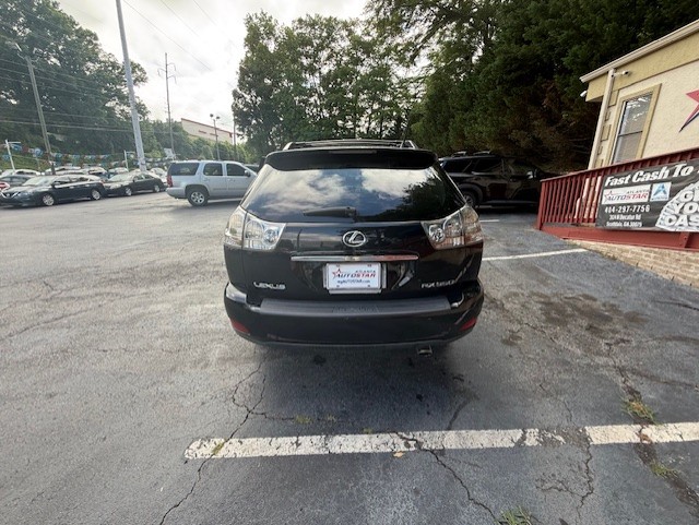 Rear view of a black Lexus SUV parked in a car lot, license plate visible, with trees and a building in the background.