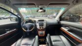 Interior of a luxury car taken from the back seats: leather seats, wood trim, center console, and a steering wheel; view of dashboard and parking lot through the windshield