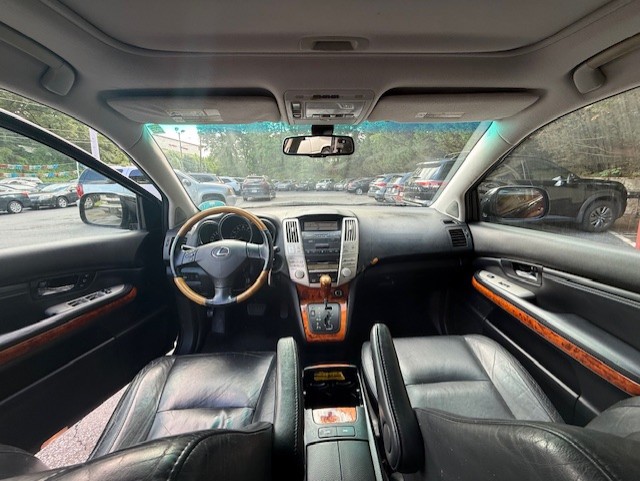 Interior of a luxury car taken from the back seats: leather seats, wood trim, center console, and a steering wheel; view of dashboard and parking lot through the windshield