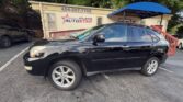 Black crossover SUV parked in front of a beige car dealership building labeled 'Atlanta Auto Star' with a blue awning and contact number above the door by the lot.