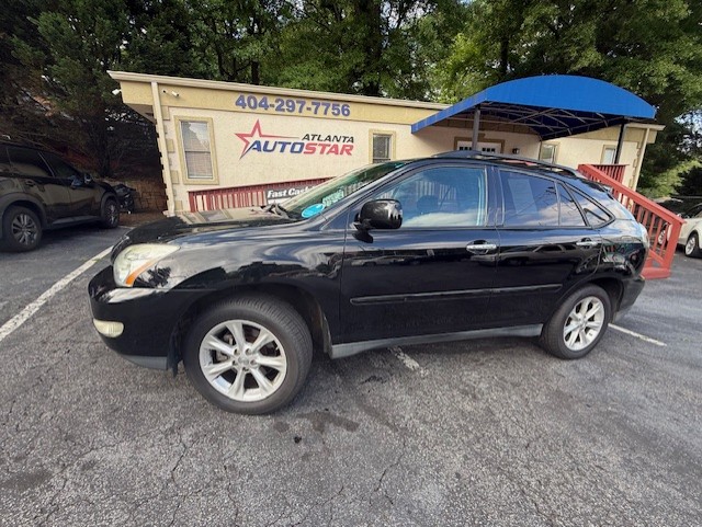 Black crossover SUV parked in front of a beige car dealership building labeled 'Atlanta Auto Star' with a blue awning and contact number above the door by the lot.