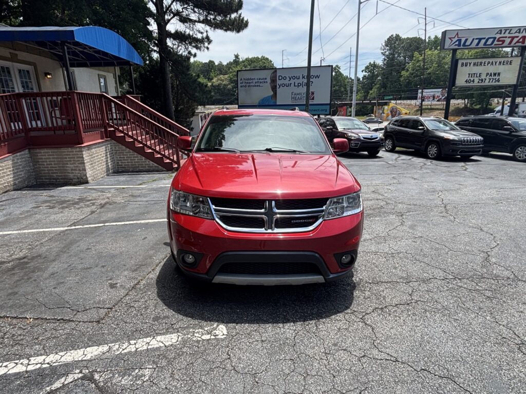 Front view of a red Dodge SUV parked in a lot, with a brick building and blue canopy on the left and other cars in the background.
