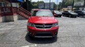 Front view of a red Dodge SUV parked in a lot, with a brick building and blue canopy on the left and other cars in the background.