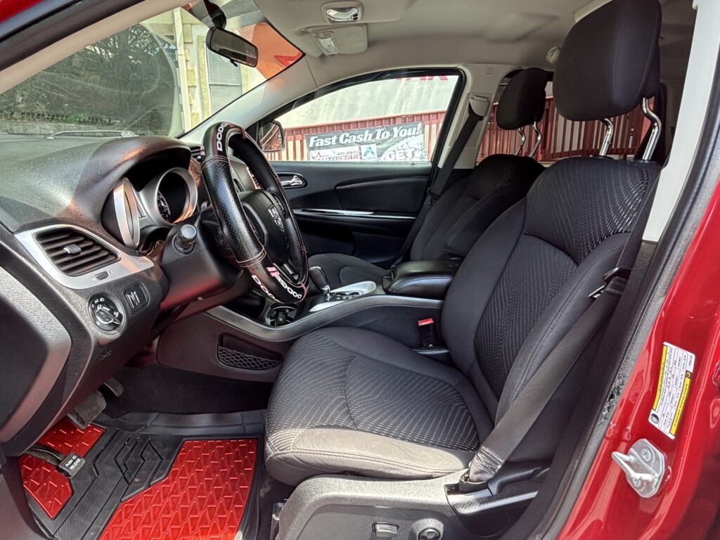 Interior of a red SUV showing the front seats, steering wheel with a cover, and bold red floor mats; a 'Fast Cash To You' sign is visible through the window outside.