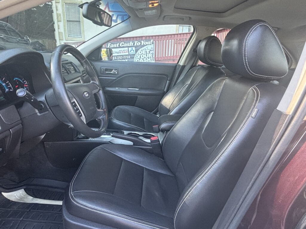 Interior of a car with black leather seats and white contrast stitching, steering wheel, and center console visible from the driver’s side door edge.