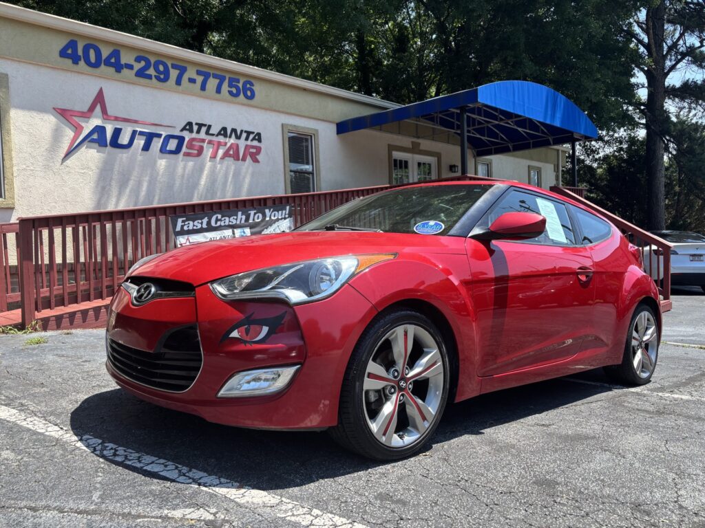 Red Hyundai sports car parked in front of Atlanta Auto Star dealership with a blue awning and banner nearby