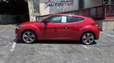 Red hatchback car parked in a lot in front of an Atlanta AutoStar dealership building with blue signage above the entrance area and a wooden ramp to the right.