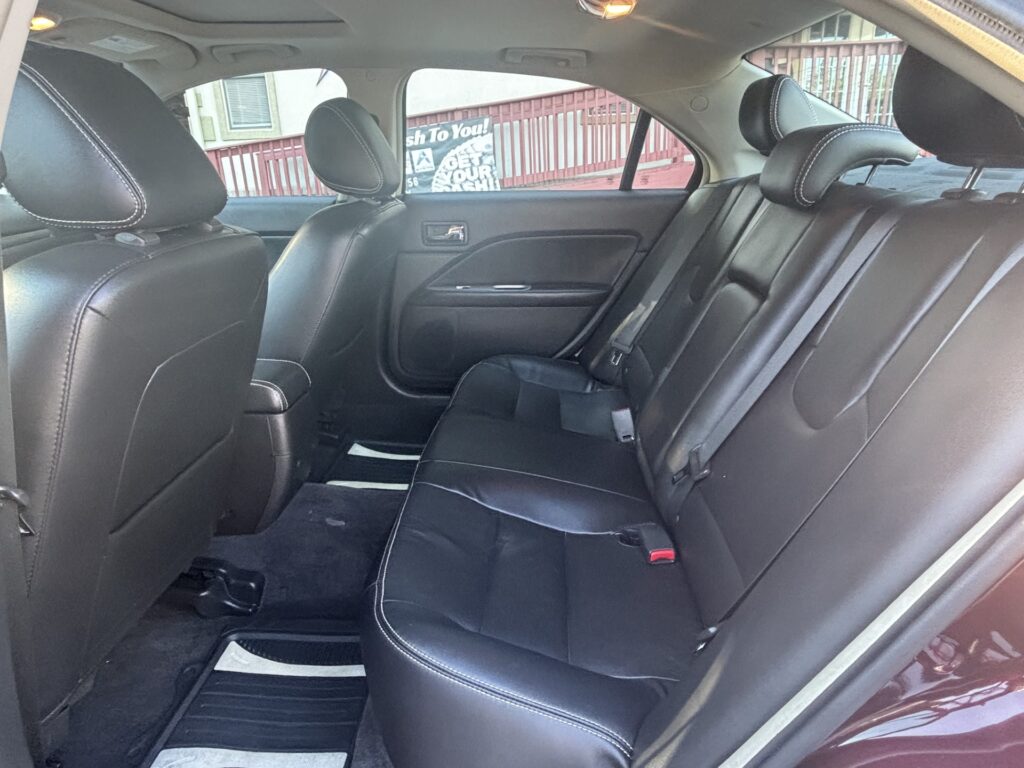 Rear seat area of a car with black leather upholstery and three headrests, viewed from the back seat window side.