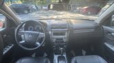 Driver's view of a car interior: steering wheel, center console, and gear shifter, with a row of parked cars visible through the windshield.