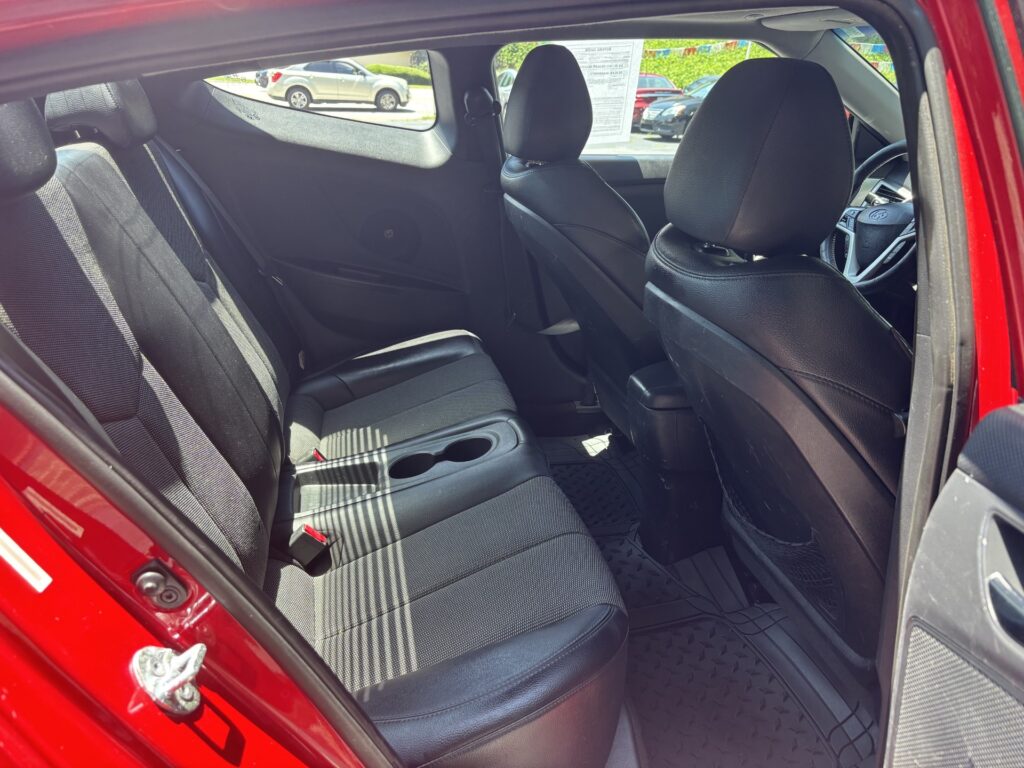 Red car interior rear seating area with black fabric seats, center console cupholders, and front seats visible from the open rear door.