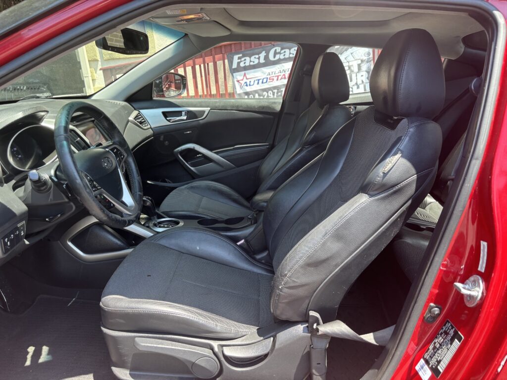 Front interior of a red car with black leather seats, steering wheel, and center console visible. A 'Fast Cash' sign is seen outside the window.