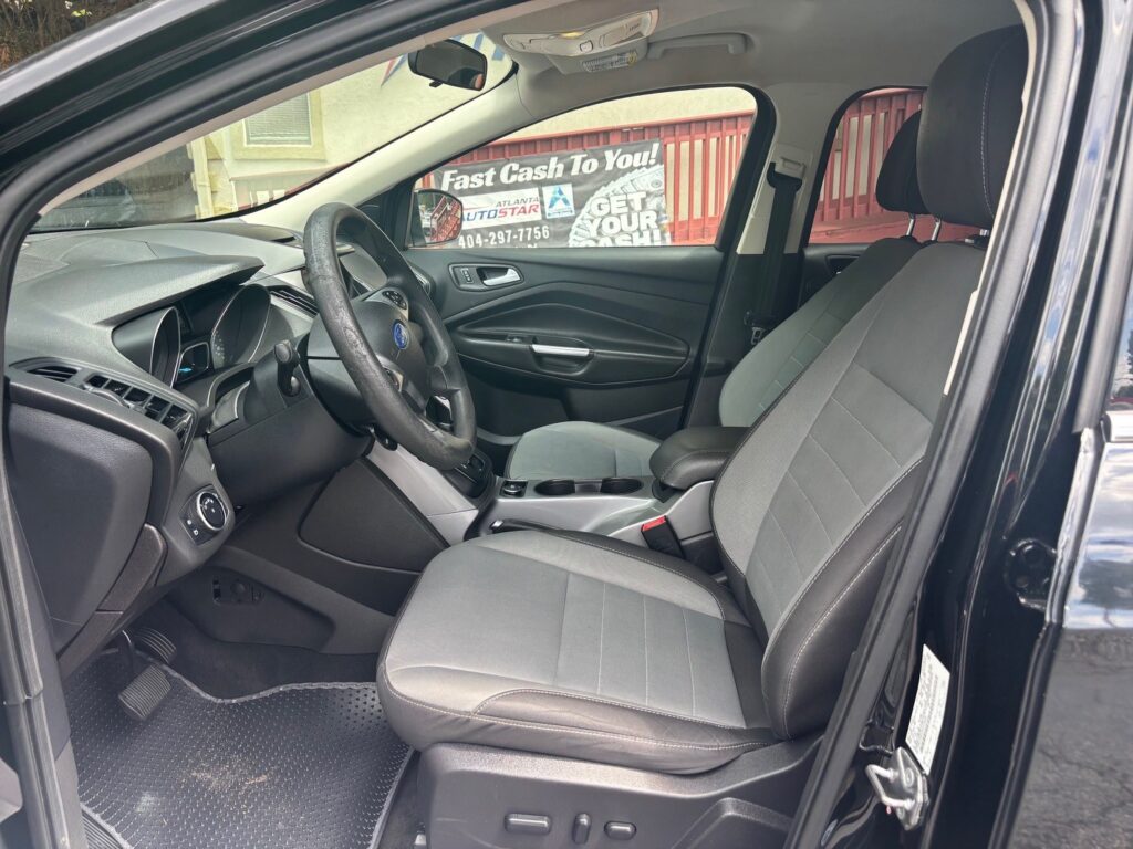 Interior of a dark SUV: driver and front passenger seats, steering wheel, center console with cupholders, and dashboard visible through an open front door.