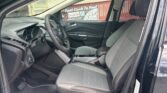 Interior of a dark SUV: driver and front passenger seats, steering wheel, center console with cupholders, and dashboard visible through an open front door.
