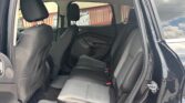 Back seat area of a black SUV with gray cloth seats, three-seat rear bench, headrests, and front seats visible; door open to outside.